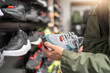 Man Shopping for Sneakers in Store, holding pair of shoes in hands.
