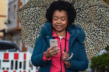 Wall Mural - afro woman on the street with umbrella using mobile phone