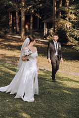 Wall Mural - A bride and groom are walking together in a grassy field. The bride is wearing a white dress and holding a bouquet of flowers. The scene is peaceful and romantic