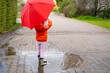 mischievous 5-year-old girl in rubber boots with red umbrella stands in rain puddle, capturing pure and simple joys childhood and magic rainy day