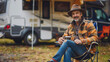 © 沈军 贡 - A handsome and casually dressed American man sits on a camping chair, holding coffee, and behind him is a complete RV