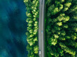 Aerial view of road between green tree forest and blue lake sea water in Finland