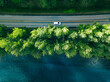 Aerial view of road between green tree forest and blue lake sea water in Finland