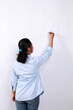 Rear view of young Asian female in blue shirt writing something on glass board with marker