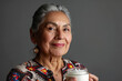 Portrait of an elderly pretty Hispanic woman with a jar of cosmetic cream in her hand on gray background. Concept of cosmetics for adult people. Silver economy concept.
