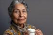 Portrait of an elderly pretty Hispanic woman with a jar of cosmetic cream in her hand on gray background. Concept of cosmetics for adult people. Silver economy concept.