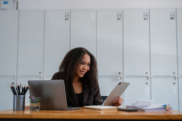 A woman is sitting at a desk with two laptops and a tablet. She is smiling and she is enjoying her work