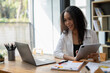 © Wasana - A woman is sitting at a desk with a laptop and tablet in front of her. She is smiling and she is enjoying her work. The scene suggests a positive and productive atmosphere