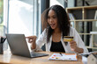 © Wasana - A woman is using a laptop to look at a credit card. She is pointing at the card and smiling