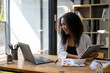 © Wasana - A woman is sitting at a desk with a laptop and tablet in front of her. She is smiling and she is enjoying her work