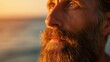 Close-up portrait of a bearded man at sunset with ocean backdrop.