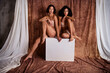 © deagreez - Full body photo of two tanned girls wearing pure beige lingerie and posing when sit podium isolated on brown background