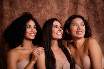 Poster - Portrait of three smiling young girls looking empty space body positivity promotion isolated on brown color background