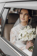 © Vasil - A bride is sitting in a car with a bouquet of white flowers. She is wearing a white dress and a veil