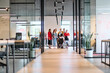 © .shock - A diverse group of young business people walking a corridor in the glass-enclosed office of a modern startup, including a person in a wheelchair and a woman wearing a hijab