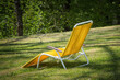 Ein gelb bespannter Liegestuhl mit weissem Metallrahmen, der auf einer Wiese in der Sonne steht