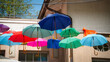 Eine bunte Sammlung von aufgespannten Regenschirmen, die an Leinen gespannt, vor einer Hauswand hängen