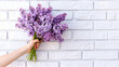 Female hand with bouquet of lilac flowers on white 