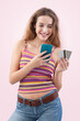 Happy and smiling young woman uses her mobile phone and credit card to browse an internet web page or online store, using her smartphone for shopping and online payments. Isolated on pink background