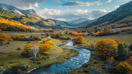 Wall Mural - A river runs through a valley with trees on both sides. The trees are orange and yellow, and the sky is blue. The scene is peaceful and serene, with the river flowing calmly through the valley