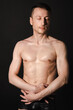 © vladorlov - A man with a beautiful body poses in the studio against a black background.