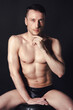 © vladorlov - A man with a beautiful body poses in the studio against a black background.