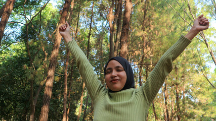 Enjoying the nature. Young muslim woman arms raised enjoying the fresh air in summer green park