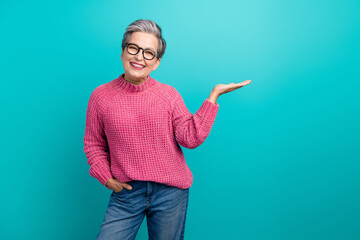 Photo of optimistic nice person dressed knit sweater in eyewear palm presenting object empty space isolated on teal color background