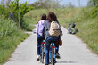 girl and her mother with a backpack on their shoulders pedaling leisurely on the cycle path in the countryside near an embankment