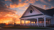 Dramatic sunset hues over a newly built clubhouse with a white porch and gable roof, featuring a semi-circle window.