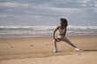 Fit black woman doing legs stretching exercise at the beach. Healthy and fitness lifestyle. Outdoor workout.