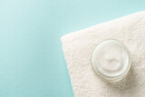 Fototapeta  - Cream jar and white towel on blue background. Skin care product. Flat lay image.