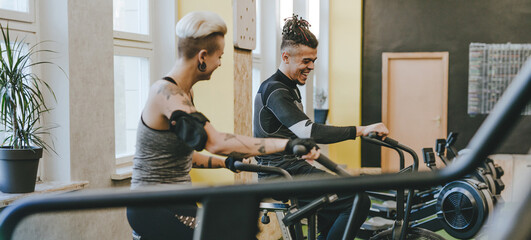 Wall Mural - Male sport trainer helping young woman riding a exercise bike during an exercise class