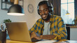 © Enigma - Cheerful african american man in casual attire enjoys listening to music on headphones while focusing on his work from a cozy home office setting