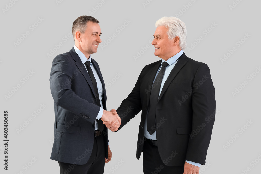 Mature brothers in suits shaking hands on grey background