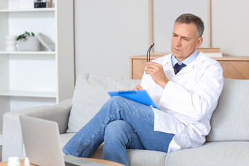 Wall Mural - Mature doctor video chatting with patient on laptop at home