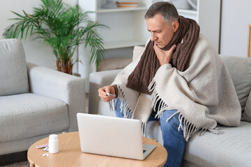 Wall Mural - Ill mature man with thermometer video chatting at home