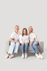 Sticker - Little girl with her mom and grandmother sitting on sofa against light background