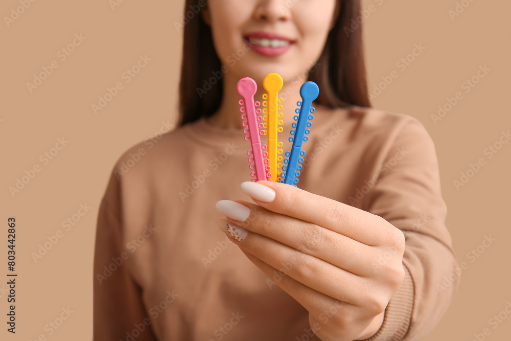 Young woman with elastic orthodontic braces on beige background, closeup