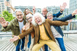 Happy group of senior people smiling at camera together outside - Delightful older friends enjoying day out walking on city street - Aged male and females pensioners hugging together outdoors