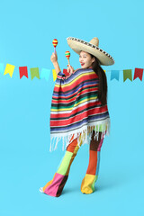 Wall Mural - Happy young woman in Mexican sombrero hat and poncho holding maracas on blue background