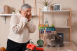 © Pixel-Shot - Shocked senior woman with cute cat and overturned flowerpot on table at home