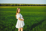 Fototapeta Łazienka - A smiling pregnant woman in a white light dress walks in a green spring garden. A woman is expecting a child. Happy pregnant woman in nature.