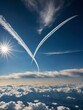 Two airplanes create white contrails as they fly across bright blue sky, leaving x-shaped lines across atmosphere. Sun shines brightly in upper left corner of frame.