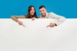 © Jose Calsina - Young adult couple pointing a blank empty board against backdrop. Advice copy space mockup. Man and woman showing a down billboard copyspace at blue color background wall. Real people presenting