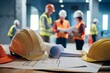 © Nida - Construction workers in helmets discuss with safety gear and blueprints amidst bustling site.