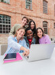 © Jose Calsina - Vertical. Group of multiracial teenage students smiling using a laptop to search information for the high school home works. Classmates studying for a exam watching the lesson on a notebook computer