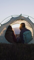 young couple of tourists look at sunset and talk. african american man sits in tent on top of hill a