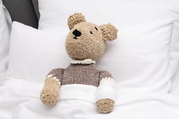 Canvas Print - Toy cute bear with bandage under blanket in bed