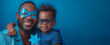 Happy African American father and son wearing matching blue outfits and superhero masks, celebrating Father's Day